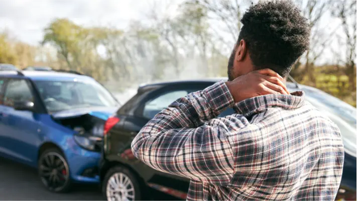 image of a person holding his neck while looking toward a crashed vehicle
